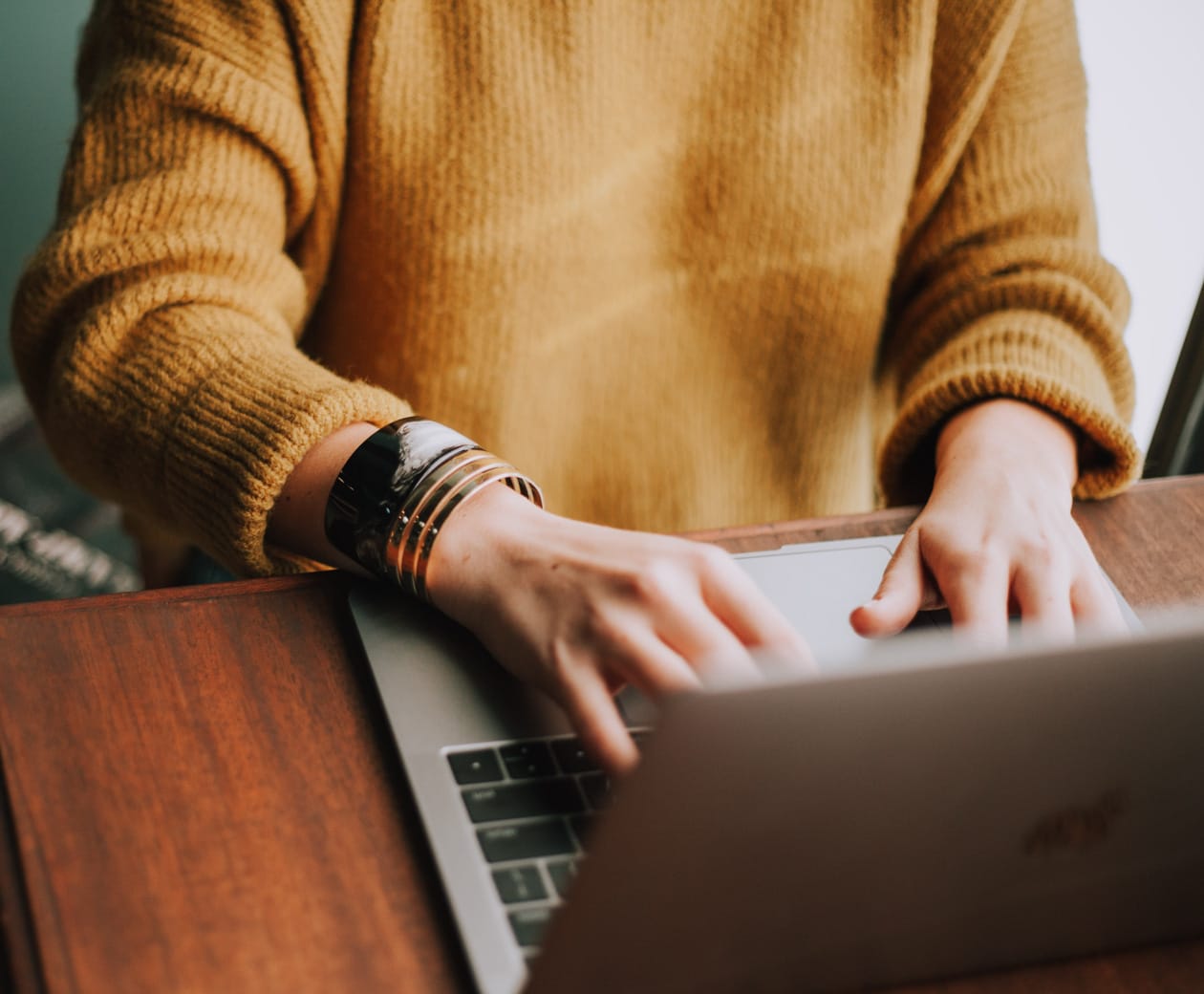 Female wearing a yellow sweater typing on laptop